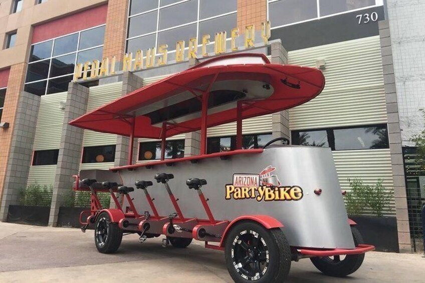 A red and silver PartyBike parked in front of a building with a sign that reads "Cigar Haus Brewery". 2