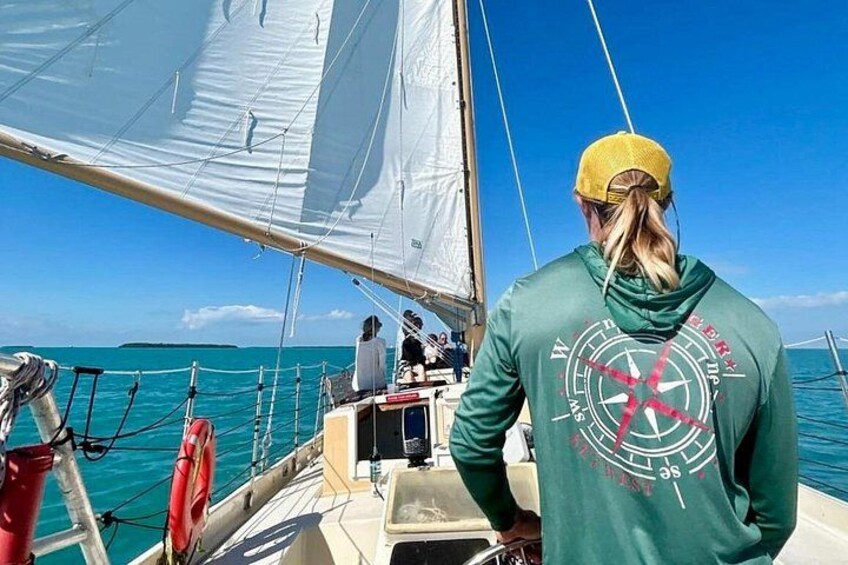 A sailboat with a person wearing a green hoodie and a yellow cap, looking out at the ocean. 1