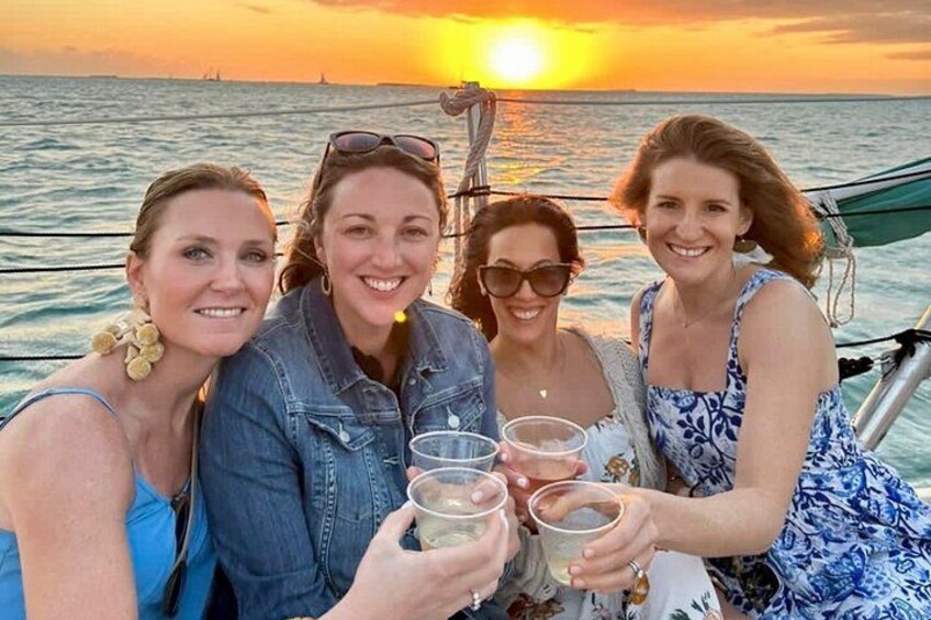 Four people toasting with drinks on a boat at sunset. 4