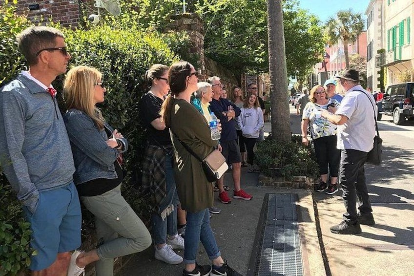 Un grupo de personas de pie en una acera, algunas sosteniendo cámaras, con edificios y árboles al fondo. 3