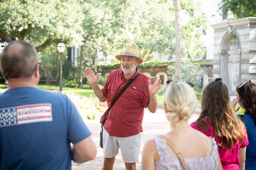 A man in a red shirt and straw hat gesturing to a group of people. 2