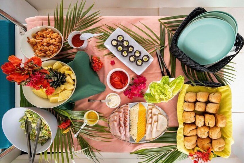 Une table décorée sur le thème des tropiques, avec différents plats, notamment des fruits de mer, du pain et des fruits tropicaux, disposés sur une nappe rose. 3
