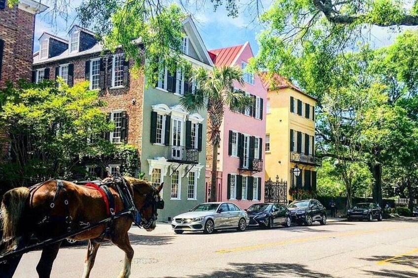 A horse-drawn carriage on a street with colorful buildings and parked cars. 1