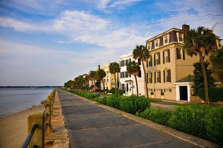 A coastal promenade with a row of historic buildings, a paved walkway, and a palm tree-lined path. 5