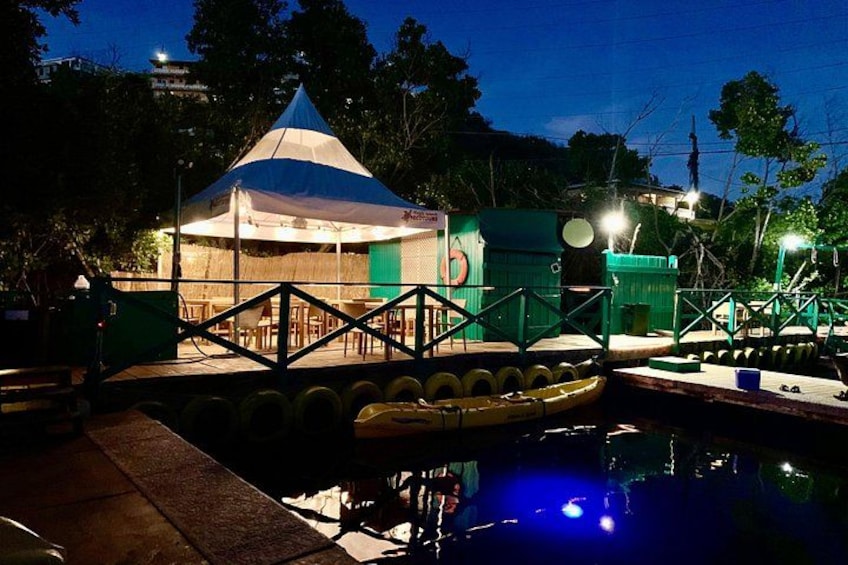 A nighttime outdoor area with a tent, a small pool, and a bridge. 4