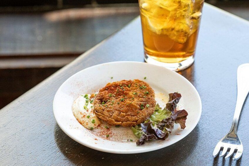 A plate with a food item, a glass of amber-colored beverage, and a fork on a wooden table. 3