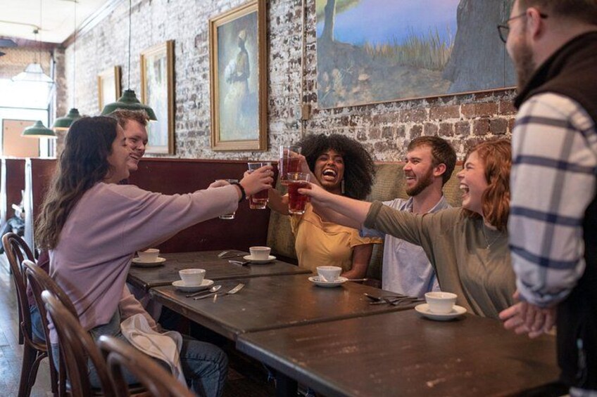 A group of people toasting with drinks at a wooden table in a restaurant with brick walls and framed pictures. 1