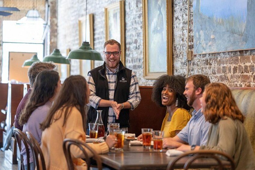A group of people seated at a table in a restaurant with a brick wall and hanging lights in the background. 5