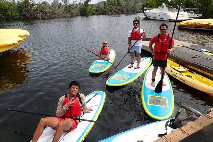 Persone su tavole da paddleboard vicino a un pontile con barche e kayak. 2