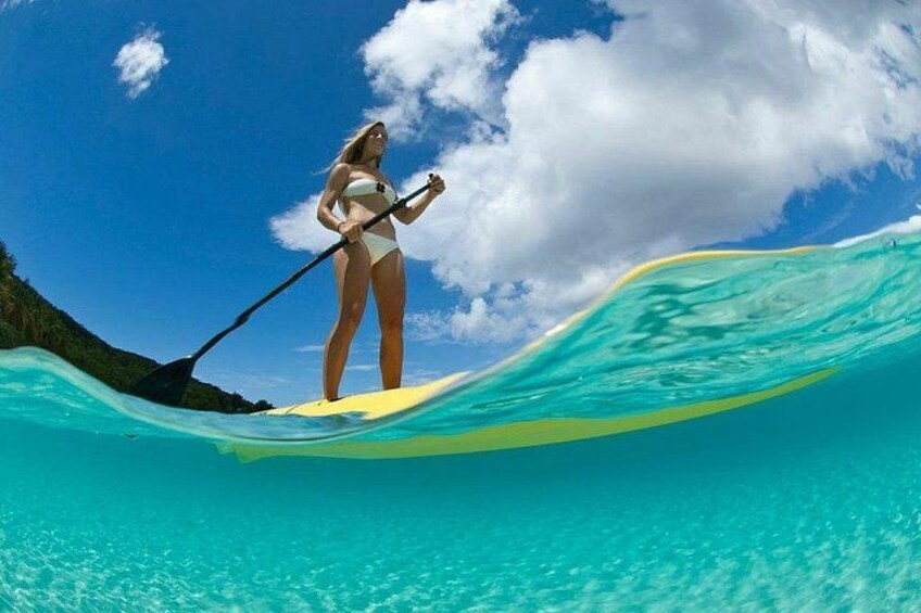Una persona fa paddleboarding su acqua turchese sotto un cielo sereno, con una terraferma visibile in lontananza. 3