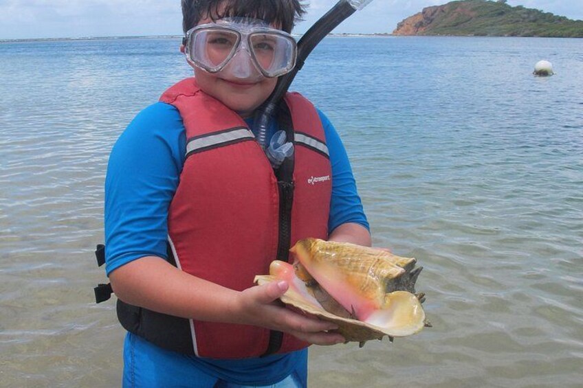 A person holding a shell by a body of water with a buoy in the background. 5