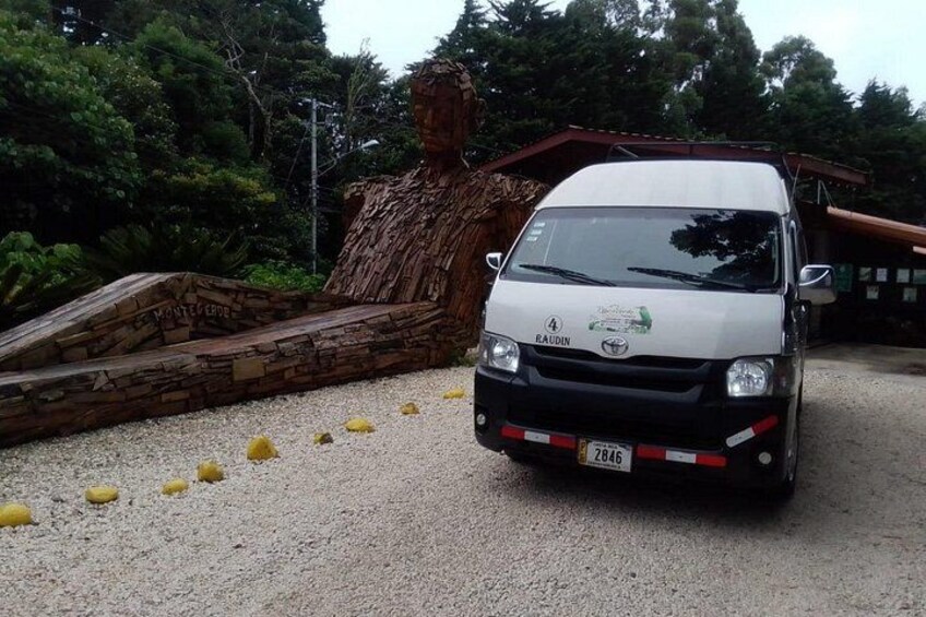 A white truck parked on a gravel surface with a wooden sculpture and greenery in the background. 2