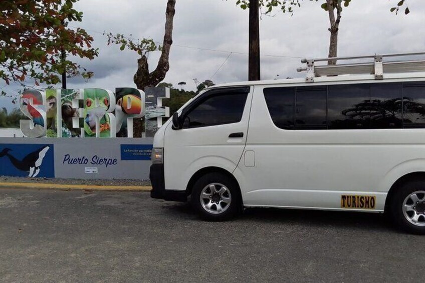 A white van parked in front of a sign with 'Puerto Sierpe' and 'Turismo' written on it. 3