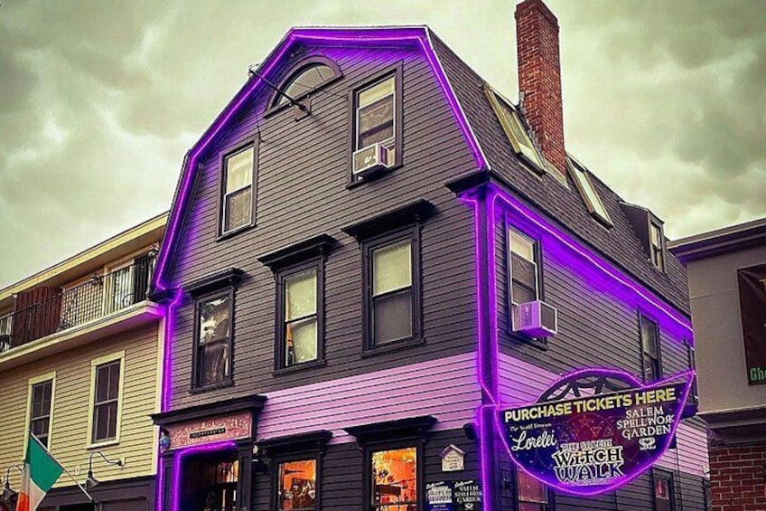 Un bâtiment illuminé de néons violets et sur lequel est affiché un panneau indiquant où acheter des billets. 1