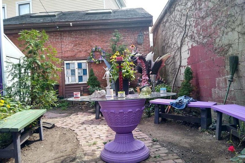 Un jardin avec une urne violette, un mur de briques et un banc en bois. 4