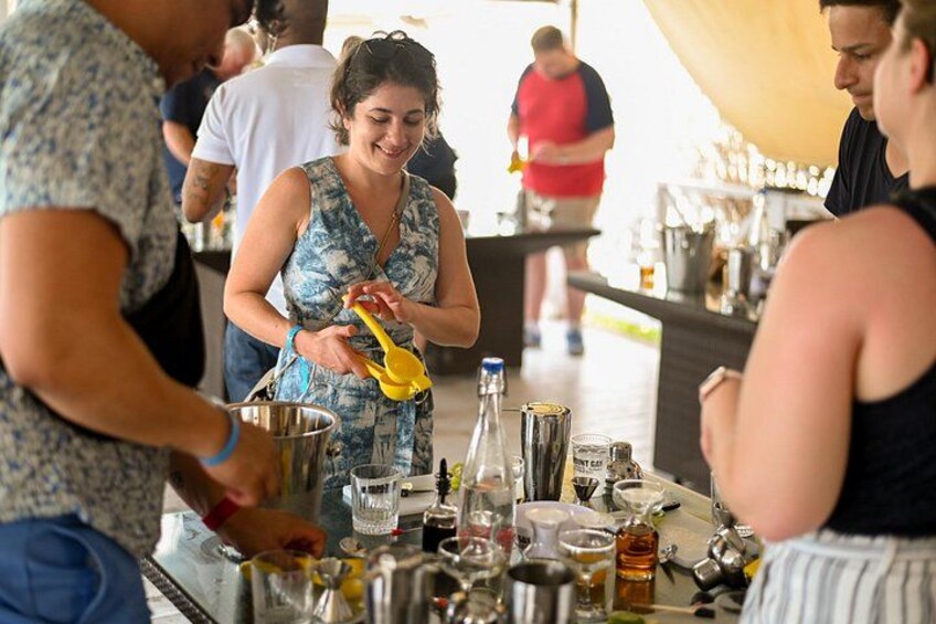 A person squeezing lemons into a glass, a bar counter with various bottles and glasses, and a crowd in the background. 1