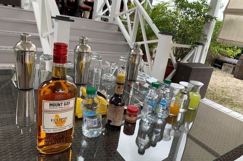 Et bord med forskellige flasker og glas, heriblandt en flaske Mount Gay rom og flere cocktailshakere. 3