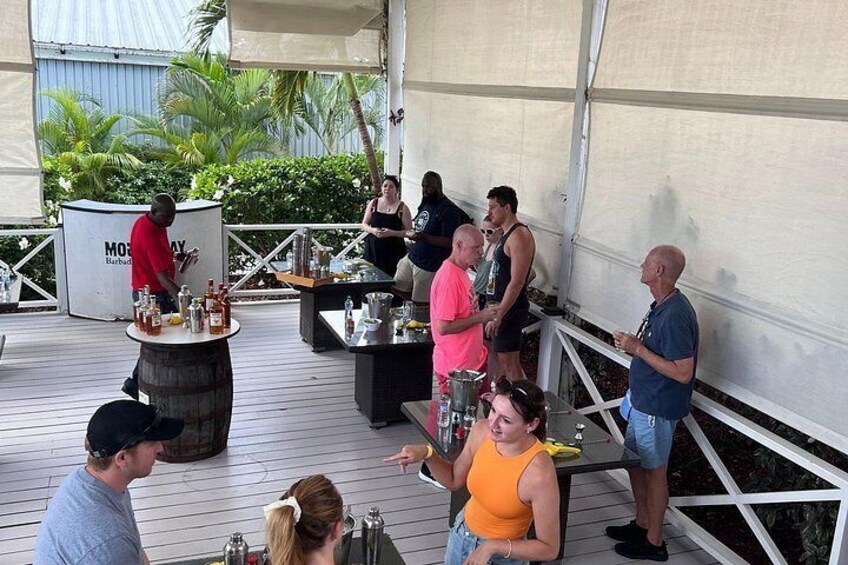 A group of people on a wooden deck with a bar area, palm trees, and a covered structure in the background. 5
