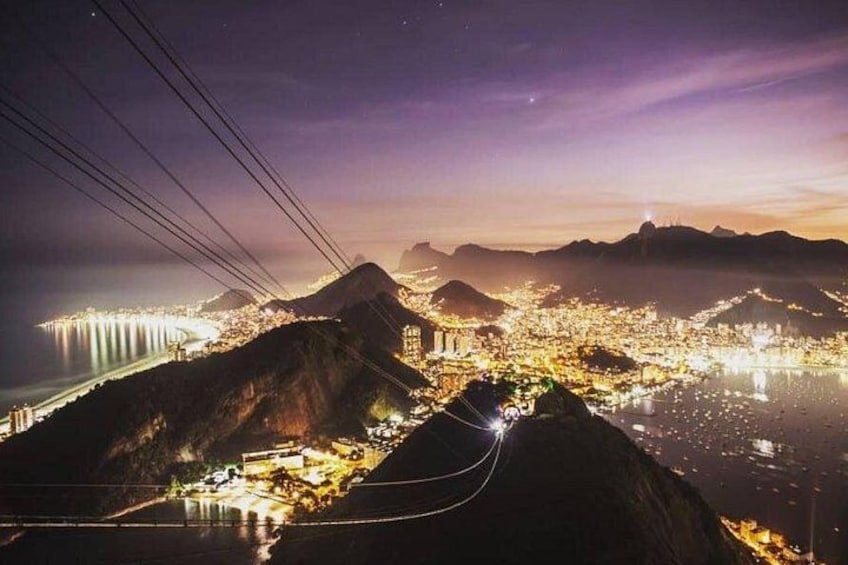 A nighttime cityscape with illuminated buildings, a river, and surrounding hills. 2