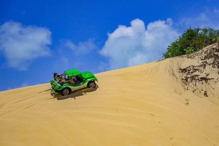 A green off-road vehicle on a sandy dune under a clear sky. 5