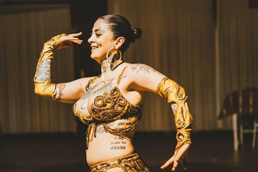 A person in a golden costume with intricate designs, performing on a stage. 1