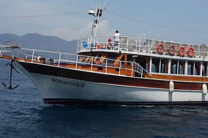A boat named WOODSTOCK H with lifebuoys on deck, anchored in calm waters with mountains in the background. 5