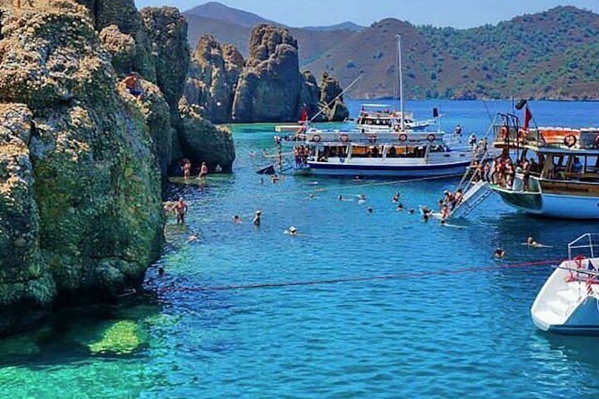 A coastal scene with clear blue water, rocky formations, and boats with people on them. 4