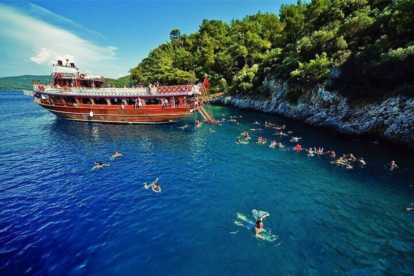 A boat with people on it, a group of people swimming in the water, and a coastline with trees. 3