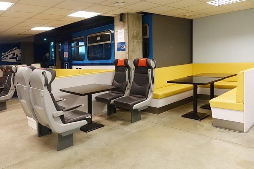 A subway station with seating areas, tables, and a train in the background. 3