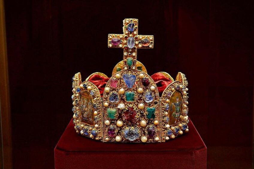 A jeweled crown with a cross on top, set on a red velvet cushion. 2