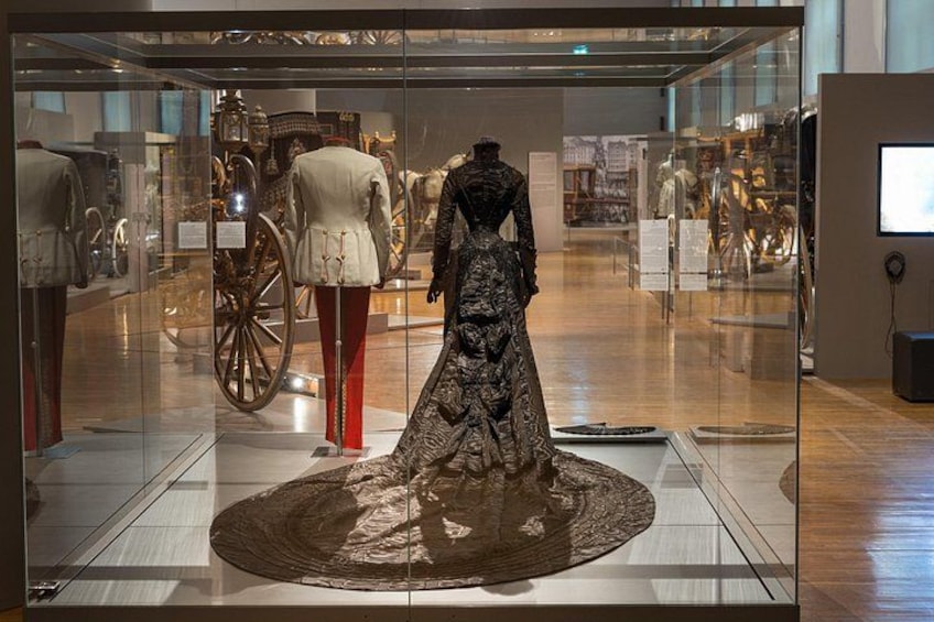 Een museumexpositie met een etalagepop in een jurk, een klassieke koets en glazen vitrines. 3