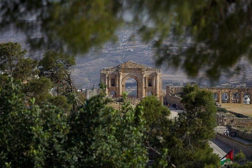 Un arc antique, avec des ruines en arrière-plan, entouré d’arbres et surmonté d’un drapeau. 4