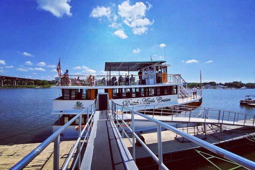 A riverboat docked at a pier with a clear sky and a bridge in the background. 3