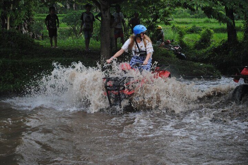 Iemand rijdt op een rode quad door een modderige beek. 2