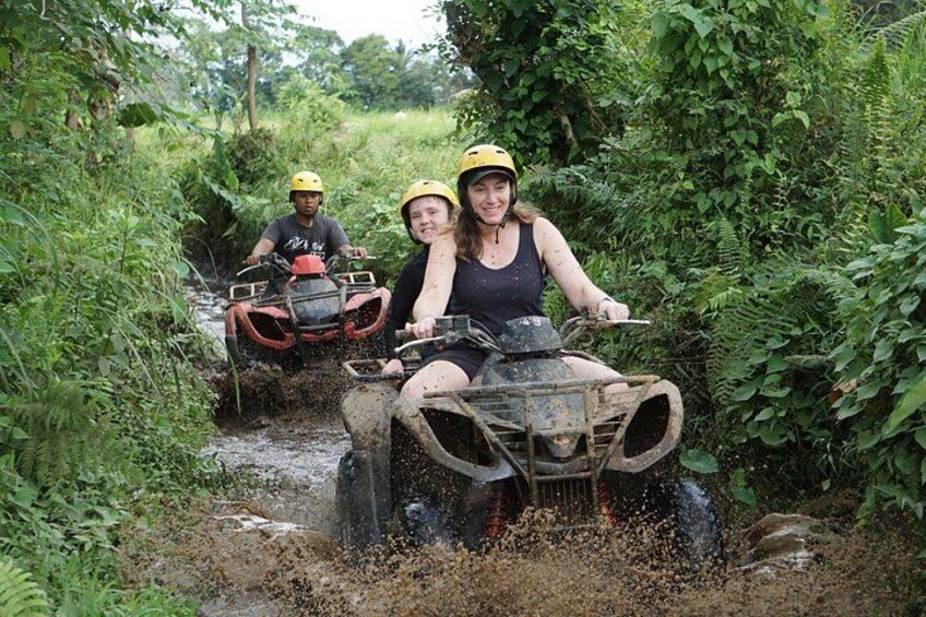 Two people on an ATV navigating through a muddy path surrounded by dense greenery. 3