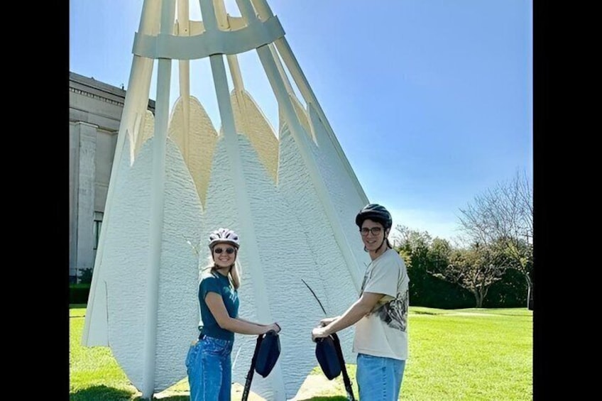 Dos personas de pie frente a una estructura blanca similar a una carpa, con un cielo despejado al fondo. 2