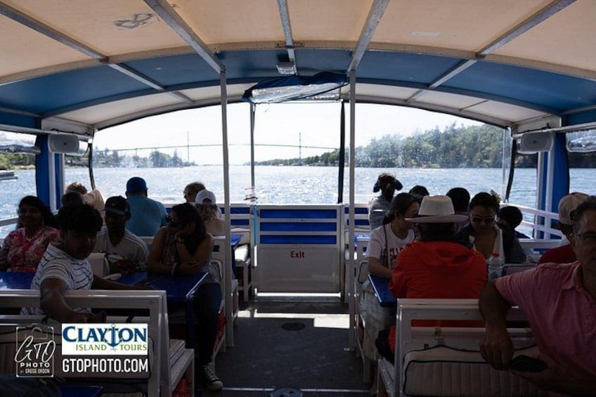 A boat tour with passengers seated under a canopy, water visible through the windows, and a bridge in the background. 3