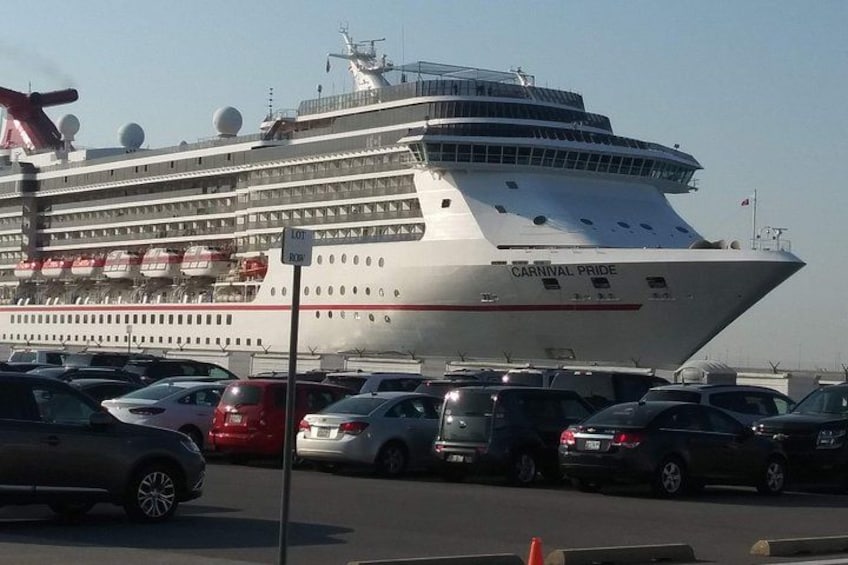Un gran crucero llamado 'Carnival Pride' atracado en un puerto, con varios coches estacionados al frente. 3