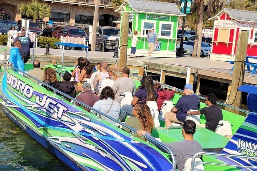 Un barco con pasajeros, atracado en una orilla con edificios y una estructura pequeña al fondo. 3