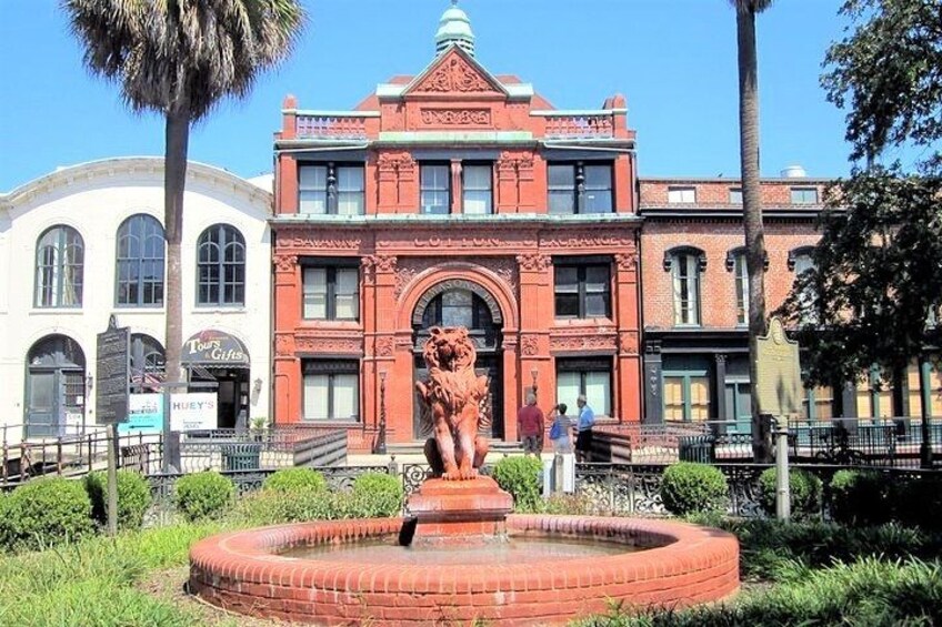 A red brick building with a lion statue in front, surrounded by greenery and palm trees. 4