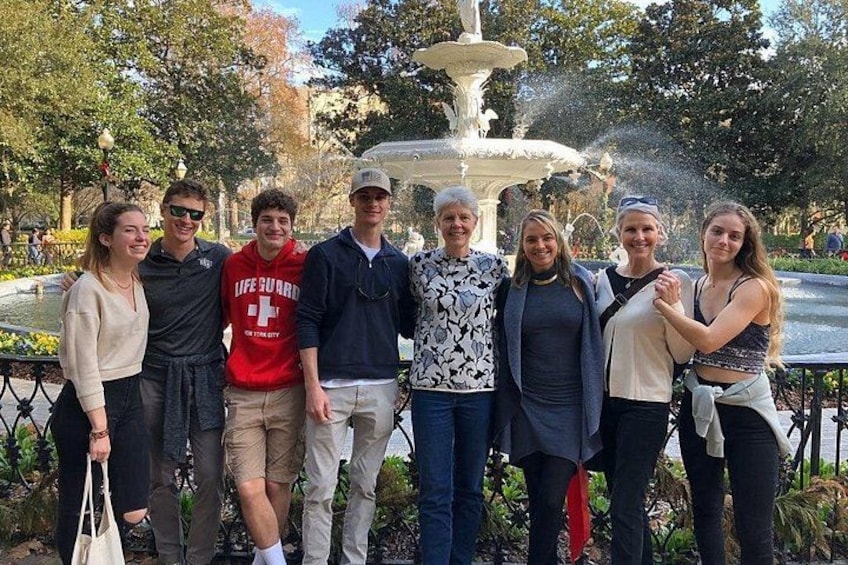 A group of people standing in front of a fountain in a park. 3