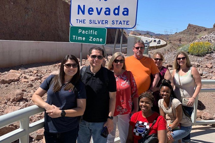 Un groupe de personnes posant devant un panneau sur lequel on peut lire « Nevada, l’État argenté » et « Fuseau horaire du Pacifique ». 2