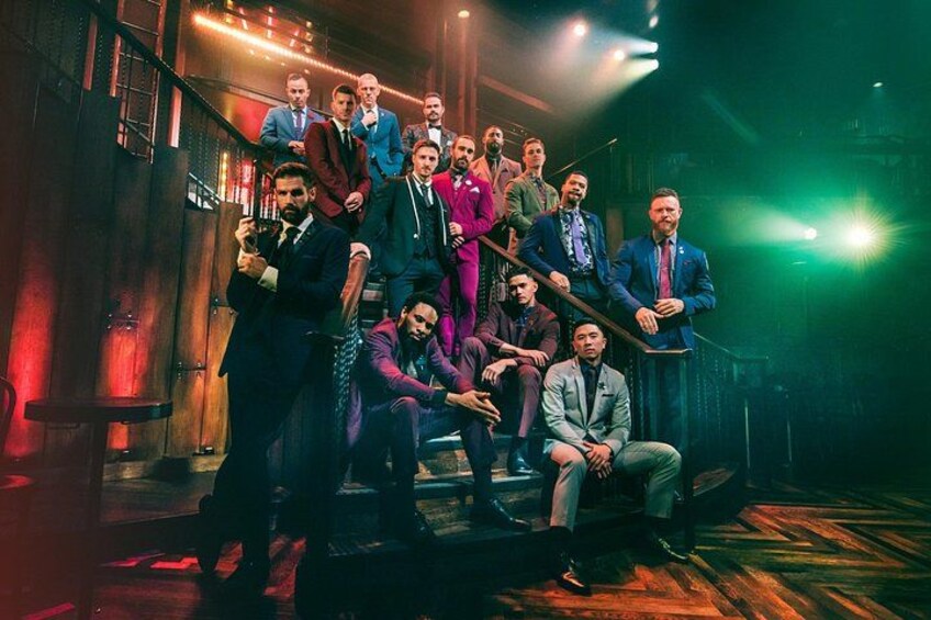 Een groep mannen in pakken op een podium met een trap en houten vloer. 2