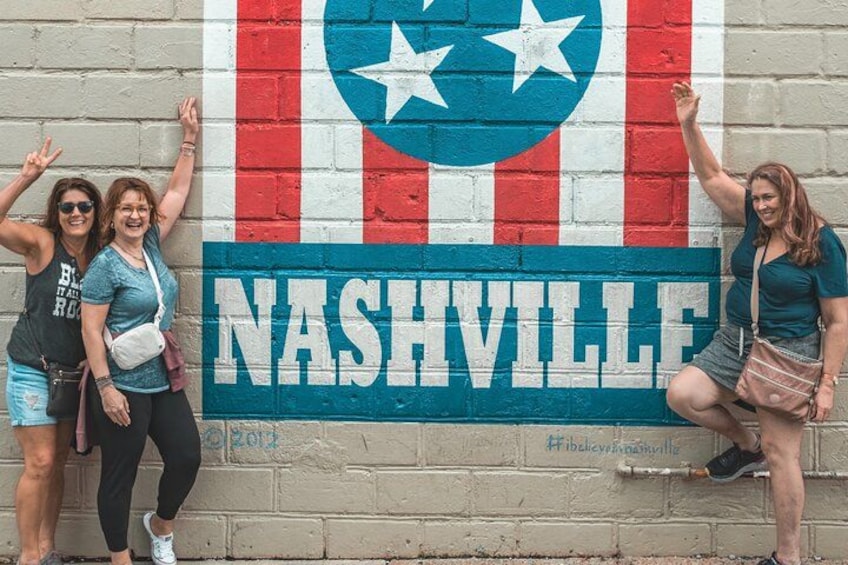 Un murale della bandiera di Nashville su un muro di mattoni, con tre persone che pongono davanti. 2