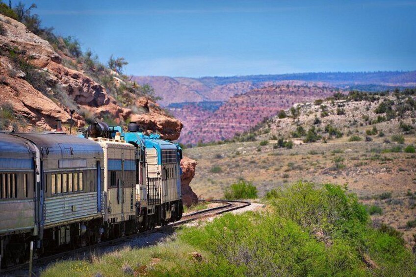 A train with caboose cars traveling through a canyon with rocky terrain and sparse vegetation. 2