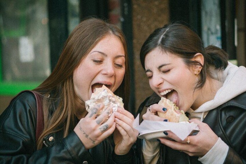 Two people eating sandwiches outdoors. 4
