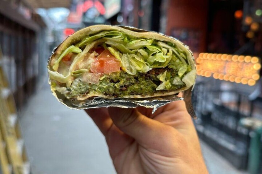 Une main tenant un burrito dans lequel on peut voir les ingrédients, comme la laitue, les tomates et une sauce verte. 4