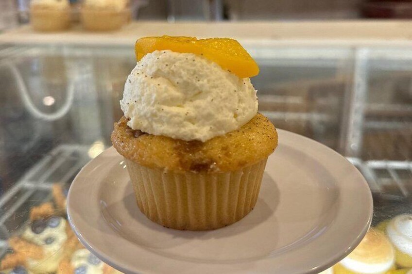 Un cupcake con una porción de helado y una rodaja de melocotón encima, sobre un plato blanco. 3