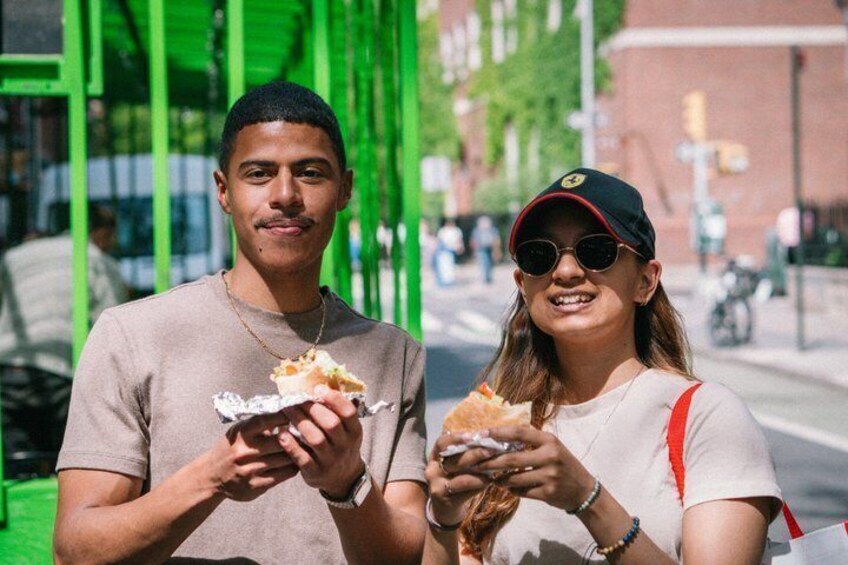 Dos personas comiendo sándwiches en una calle. 1