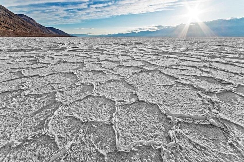 A salt flat with cracked ground and distant mountains under a clear sky. 1